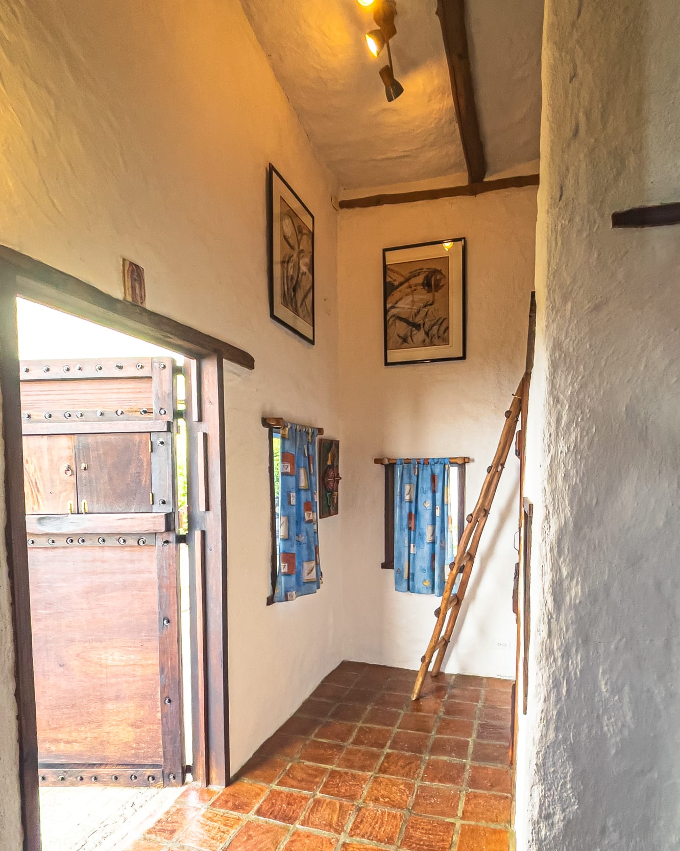 Recibidor de piso de arcilla con la puerta claveteada abierta y dos cuadros enmarcados en la pared