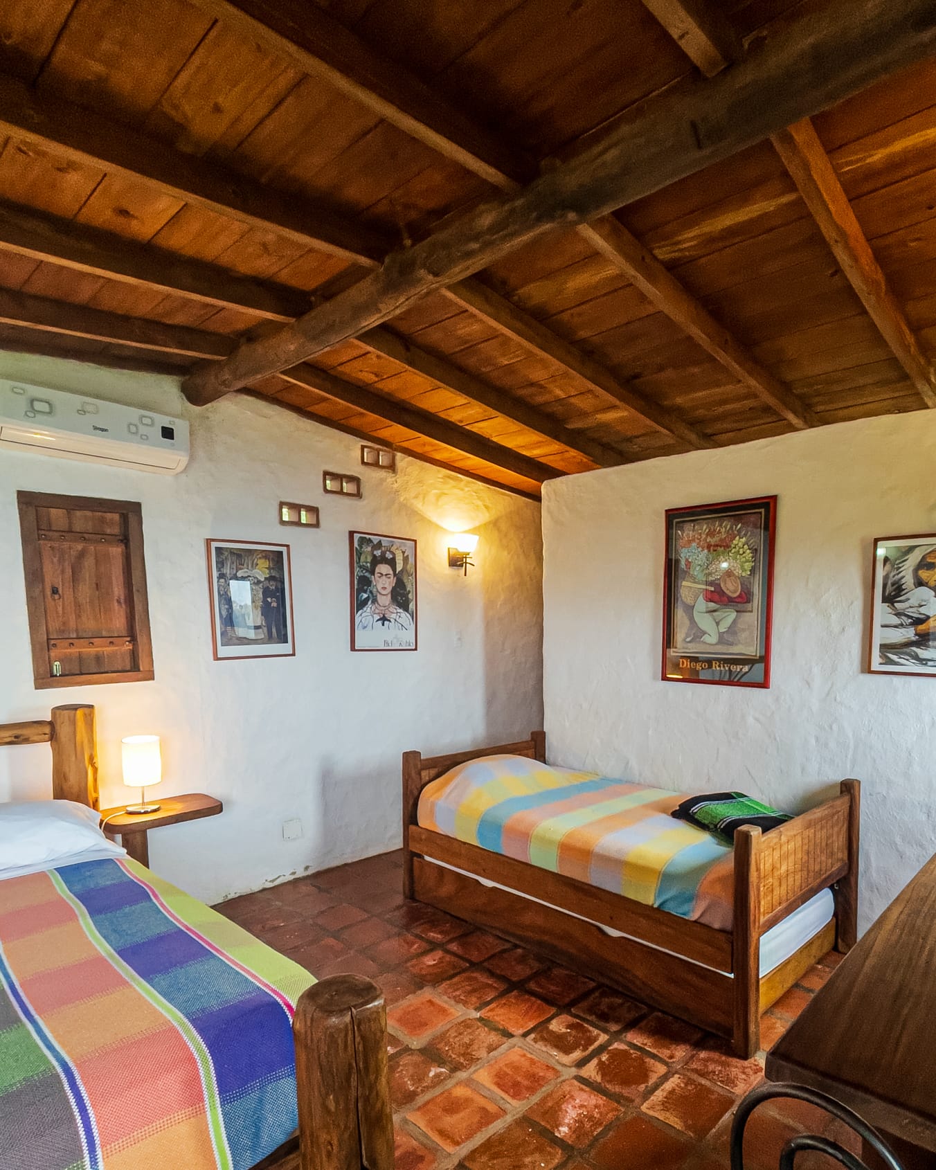 Entre afiches de Frida Kahlo y Diego Rivera, una cama individual con cobija a rayas sobre el piso de arcilla