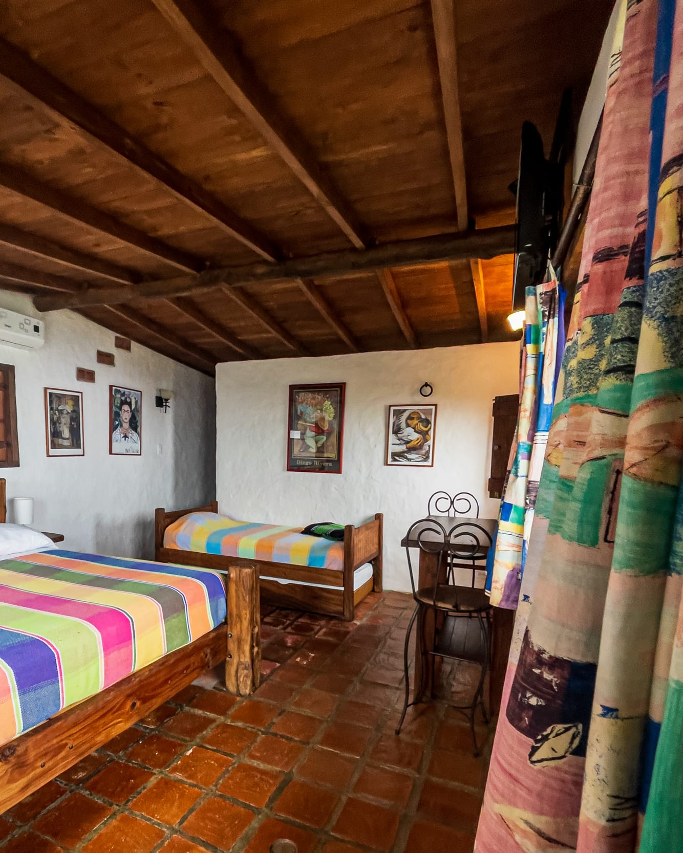 Desde la cama grande se ve la individual del fondo, con una mesita de hierro y la cortina estampada a un lado