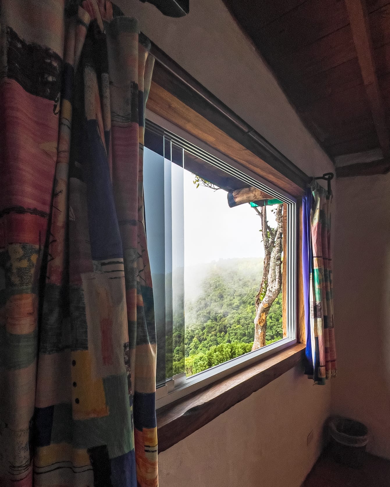Neblina sobre el bosque de Galipán tras la ventana panorámica, entre cortinas de retazos de colores