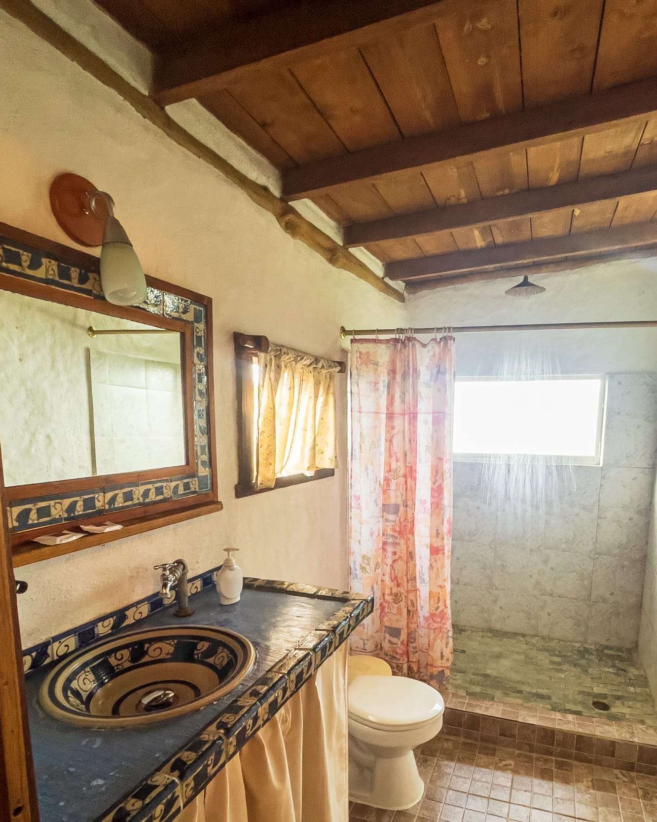Lavamanos de cerámica pintada, espejo con cenefa de azulejos y ducha de piedra tras la cortina