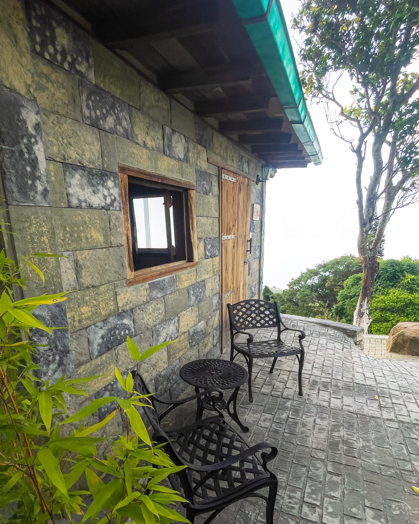 Dos sillas de hierro y una mesita esperan en la terraza adoquinada, junto al muro de piedra y la neblina del Ávila