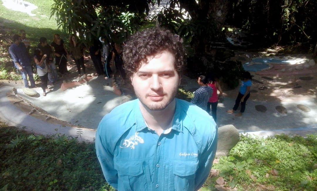 Guía joven de camisa azul frente a un grupo de visitantes en los senderos de piedra de un jardín en Galipán