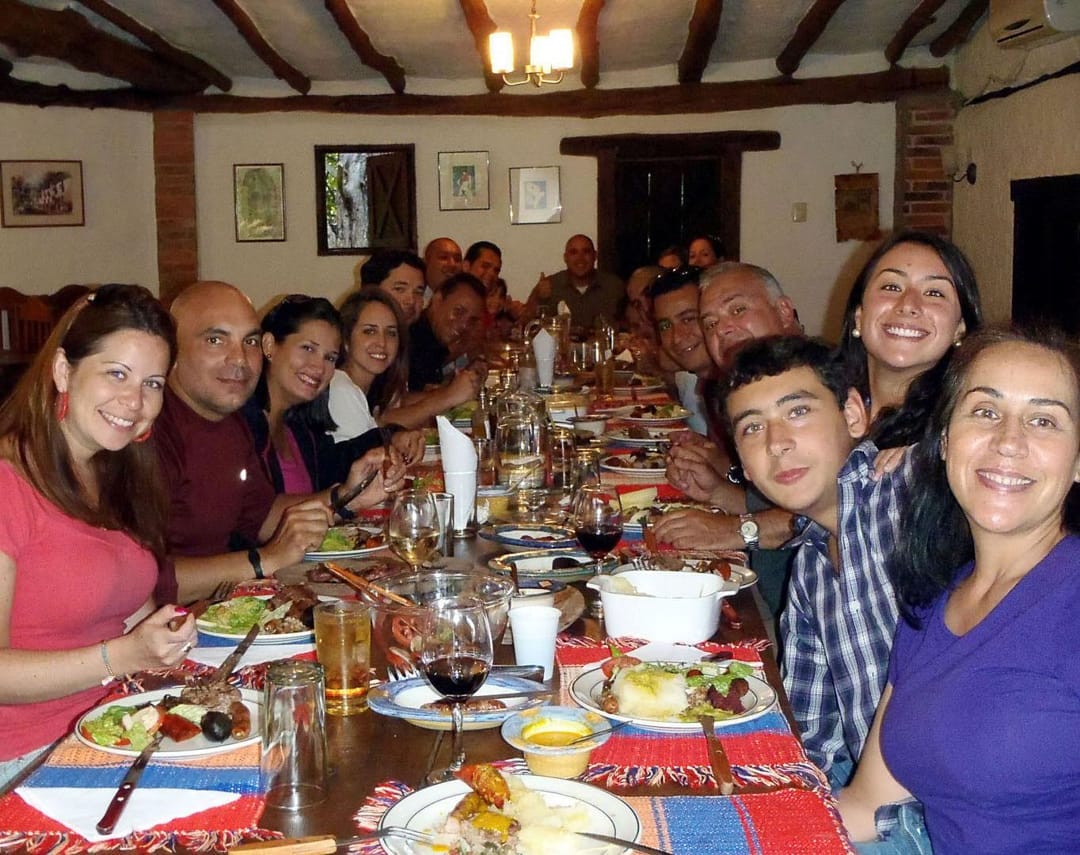 Familia numerosa cena y sonríe alrededor de una mesa larga bajo el techo de vigas del Restaurante Tarahumara, Galipán.