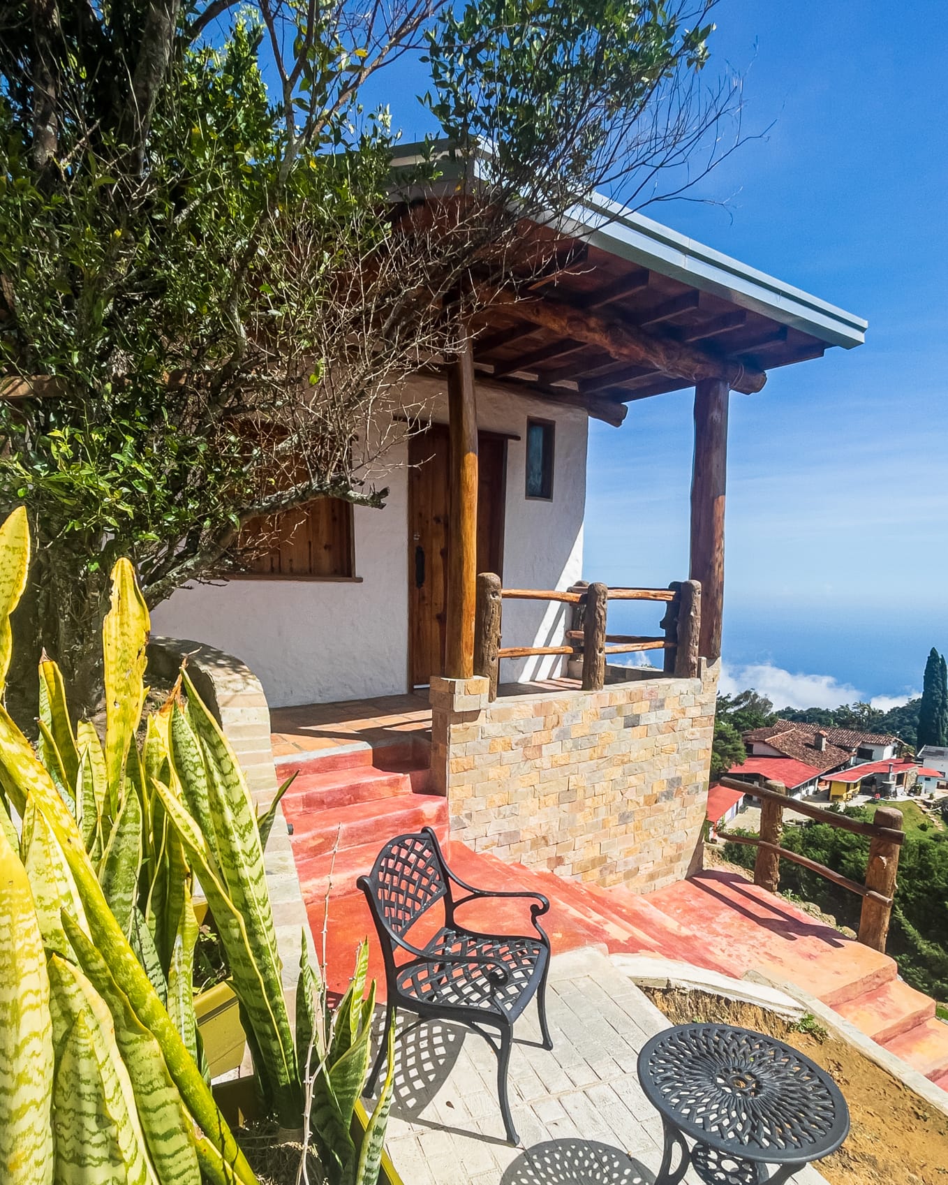 Entrada de la Cabaña Lilaila con escaleras rojas, porche de troncos y el mar Caribe al fondo