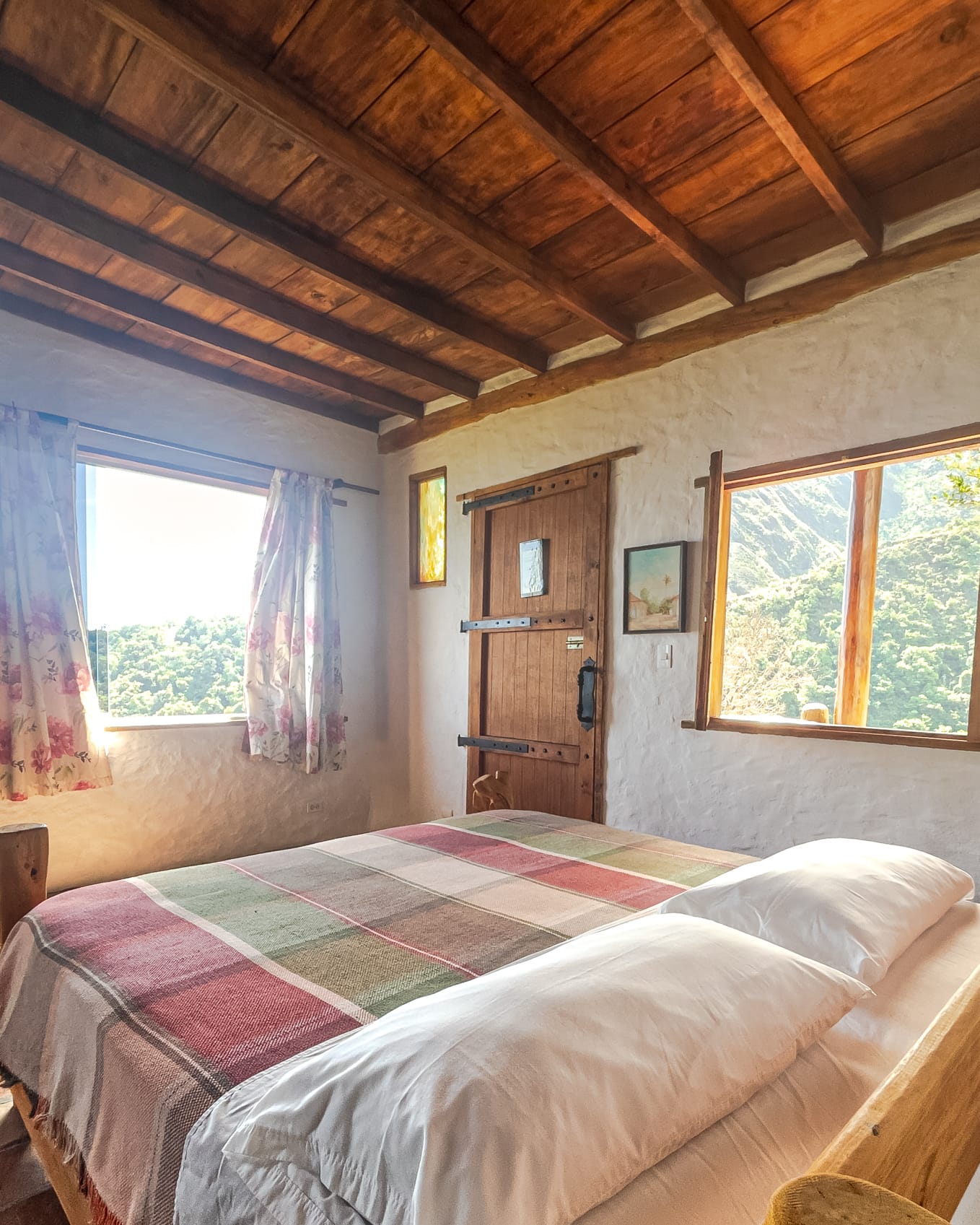 La cama arropada con manta tejida frente a la ventana que enmarca el verde del Ávila