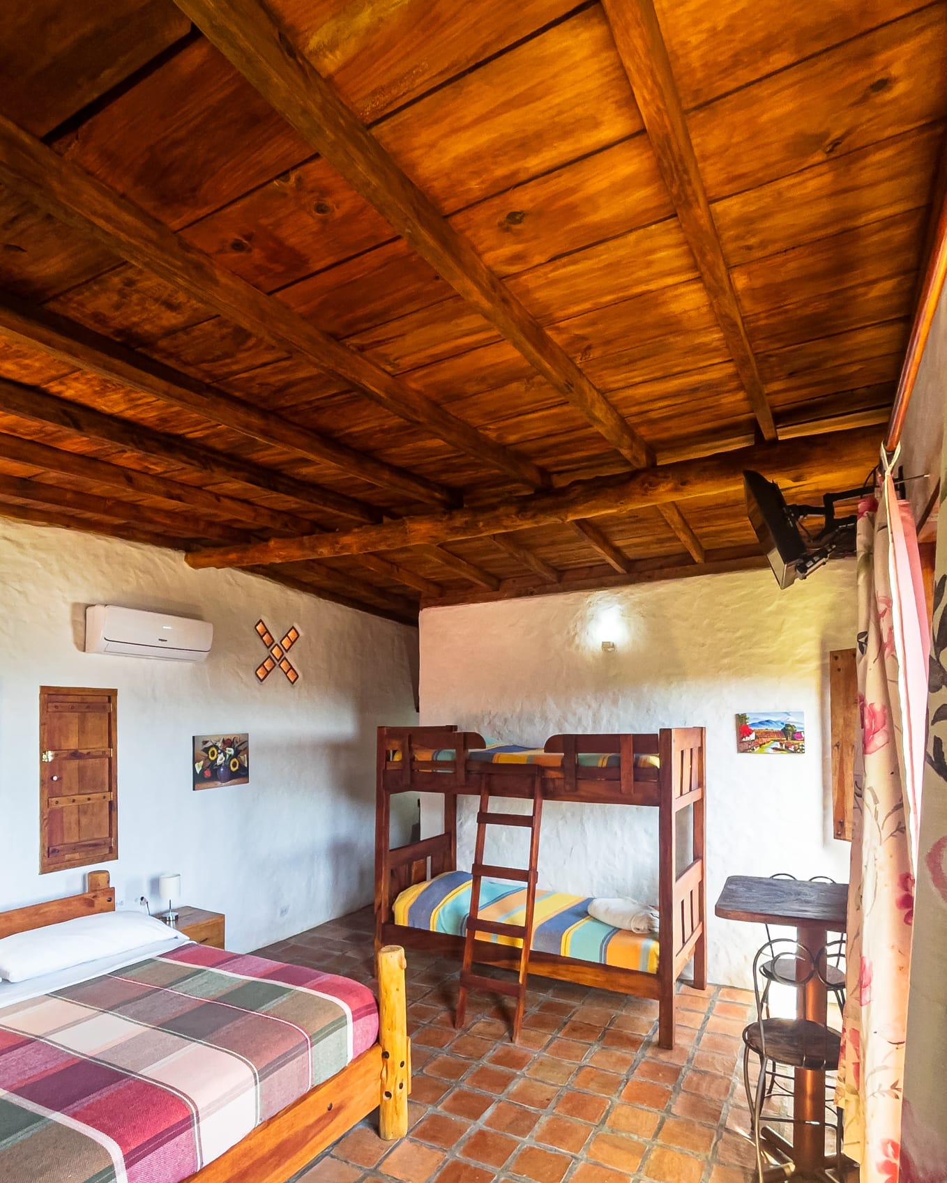Litera de madera con colchas de colores junto a la cama principal y una mesa alta con banquitos