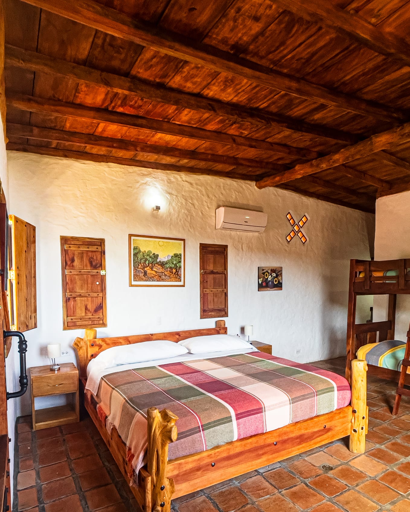 Amplio dormitorio de piso de terracota con cama king, mesita con lámpara y litera a un lado