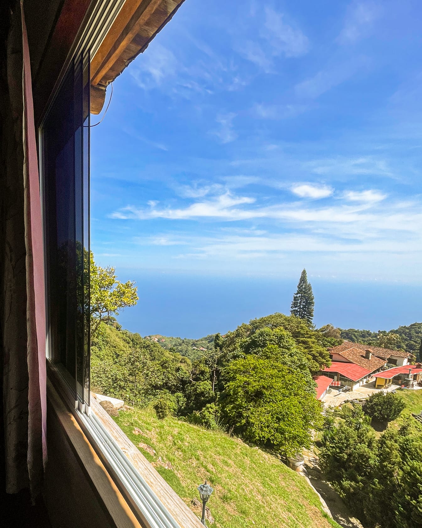 Ventana abierta al azul del mar Caribe, con un ciprés que sobresale entre el verde