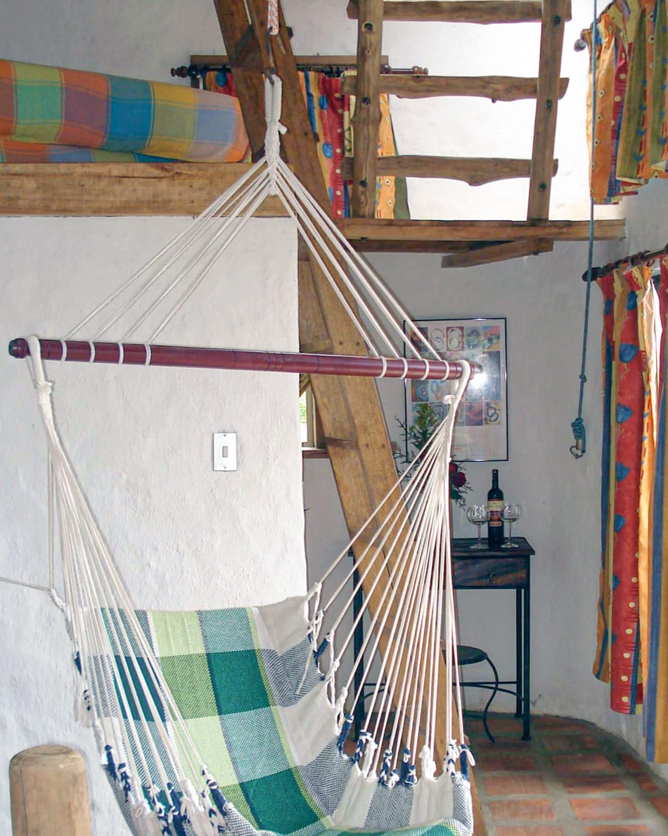 Silla hamaca junto a la escalera de troncos que sube al altillo, con una botella de vino y dos copas en la mesita