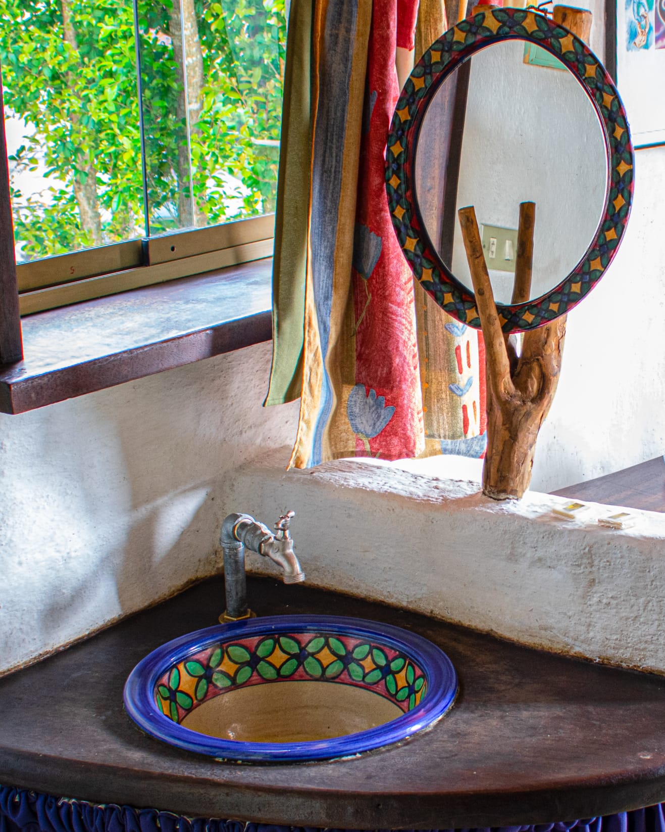 Detalle del lavamanos de talavera con grifo antiguo y espejo redondo sostenido por una rama de madera