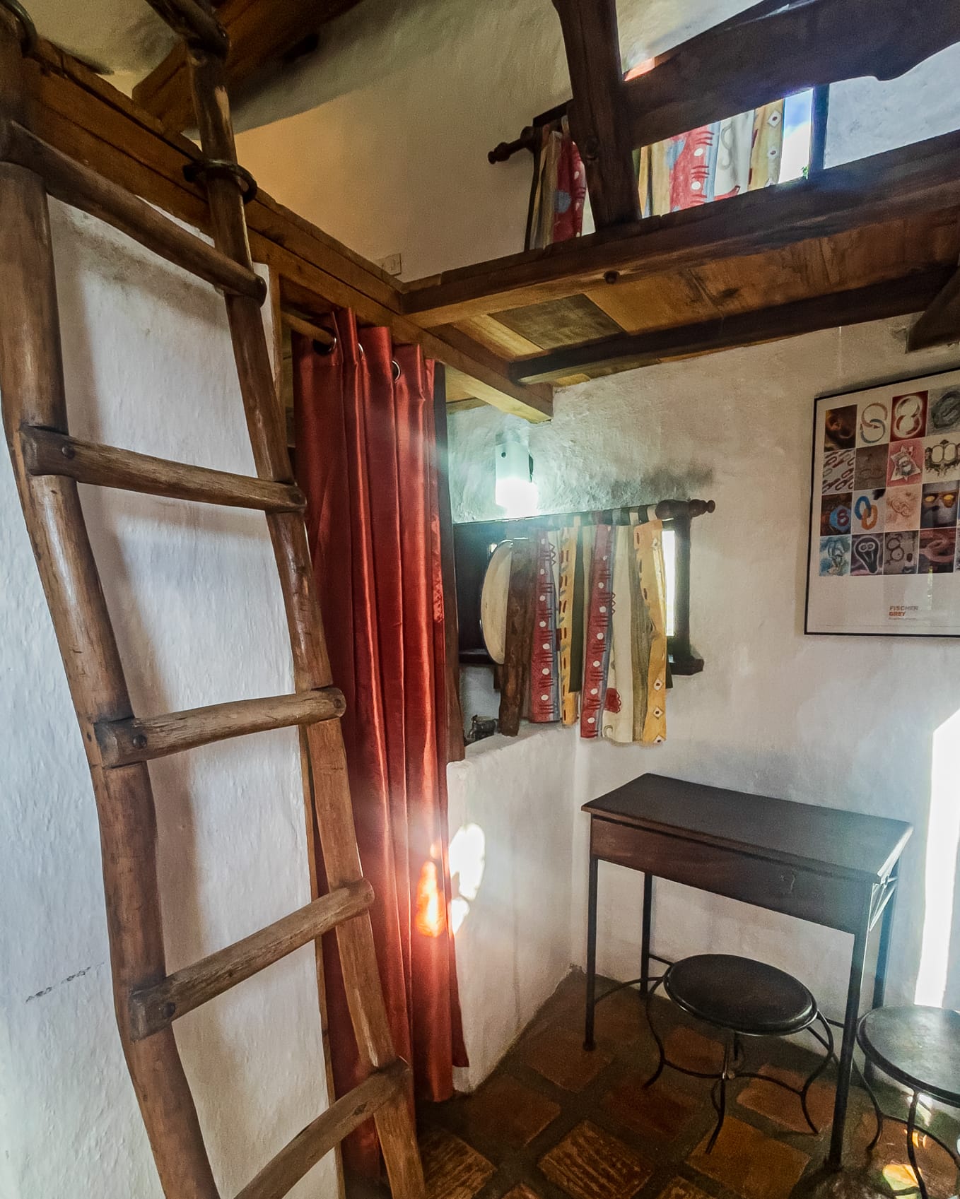 Rincón de escritorio con dos banquitos de hierro al pie de la escalera de madera que sube al nivel de arriba