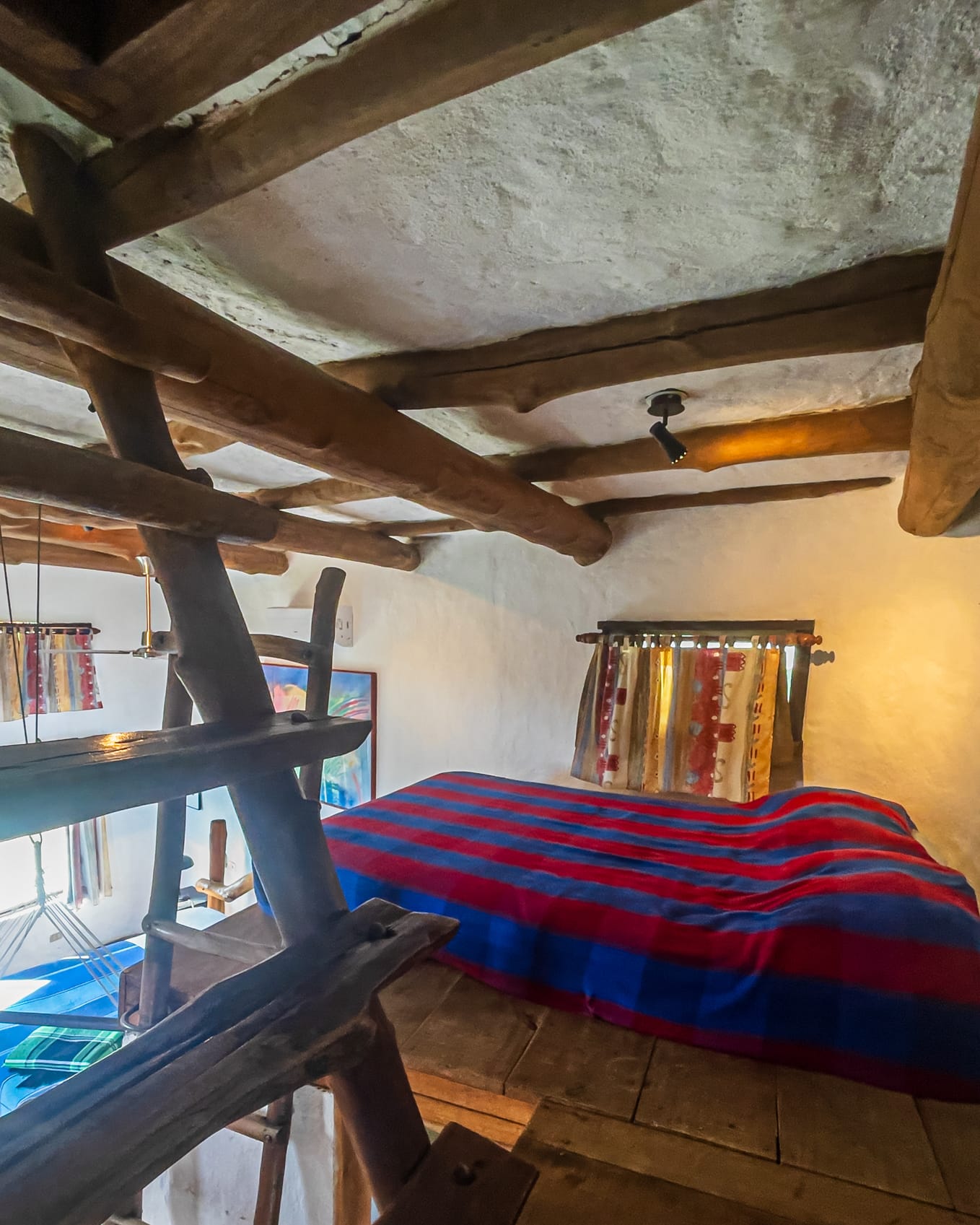 Altillo bajo las vigas gruesas con la cama matrimonial de rayas rojas y azules sobre un piso de tablones