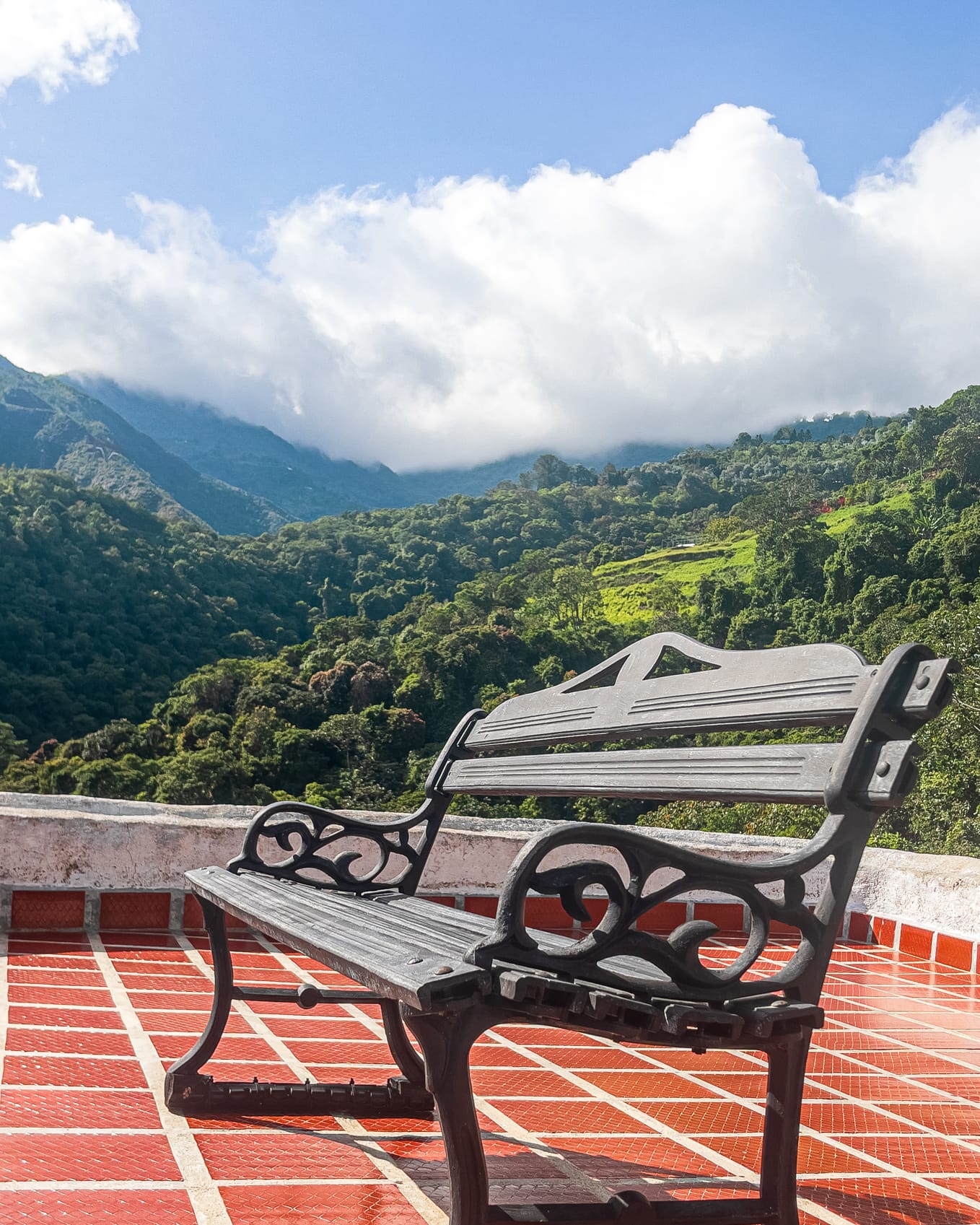 Banco de hierro forjado en la terraza de terracota frente a las montañas nubladas del Ávila
