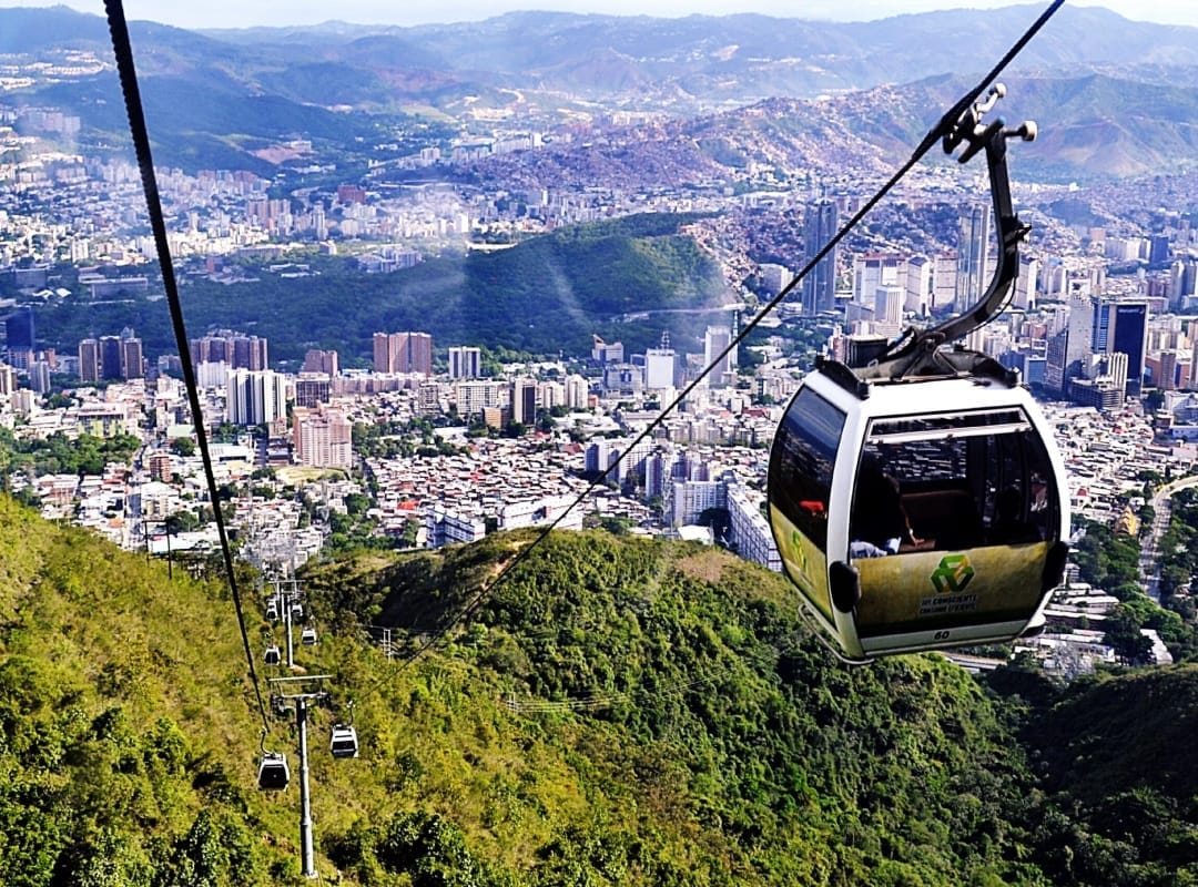 Cabina del teleférico Warairarepano suspendida sobre la montaña verde, con la ciudad de Caracas al fondo