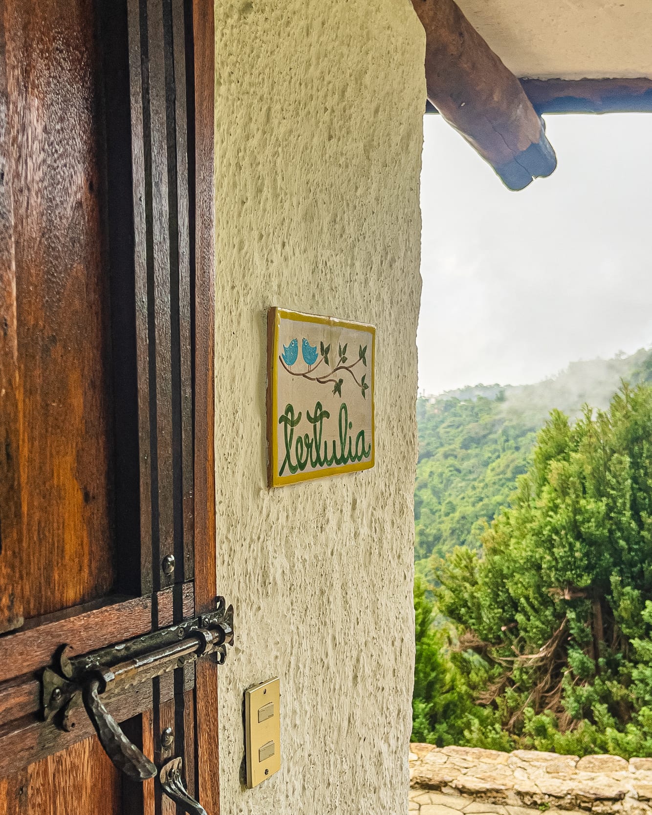 Placa de cerámica con el nombre Tertulia y dos pajaritos azules junto al portón de madera, con la niebla al fondo