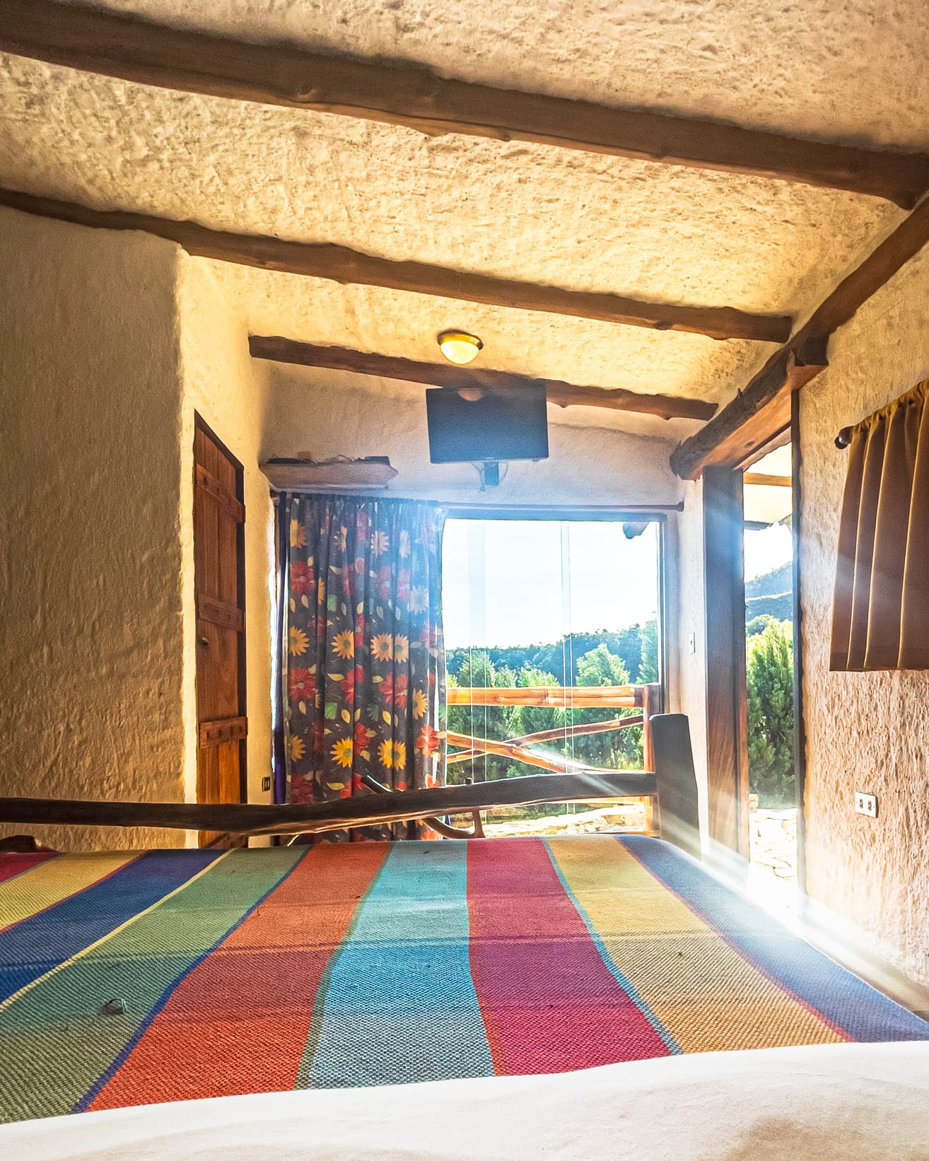 El sol entra por el ventanal hasta la cama de rayas multicolores, entre cortinas floreadas y vigas encaladas