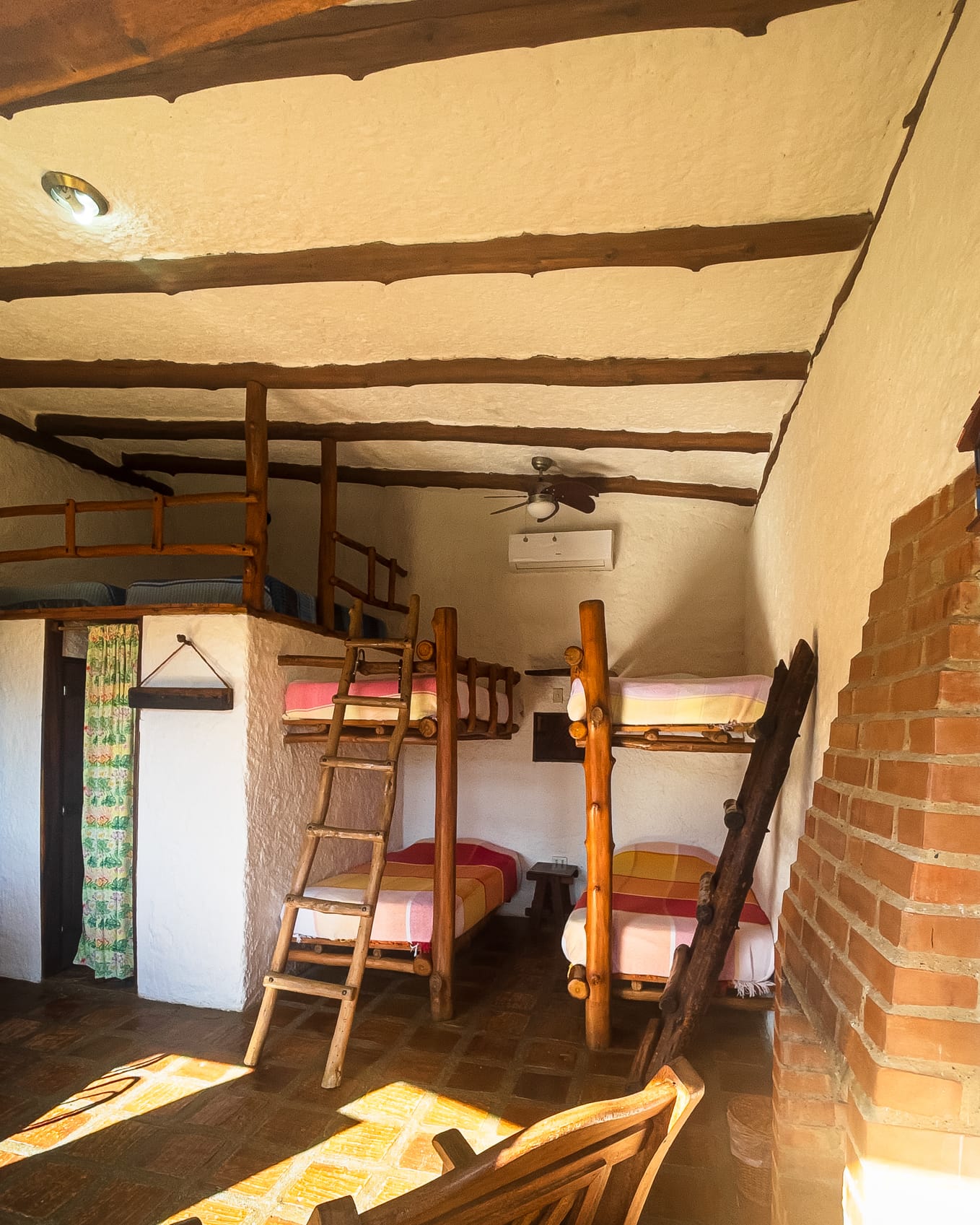 Literas de madera con cobijas de colores junto a la chimenea de ladrillo, con aire acondicionado y altillo arriba