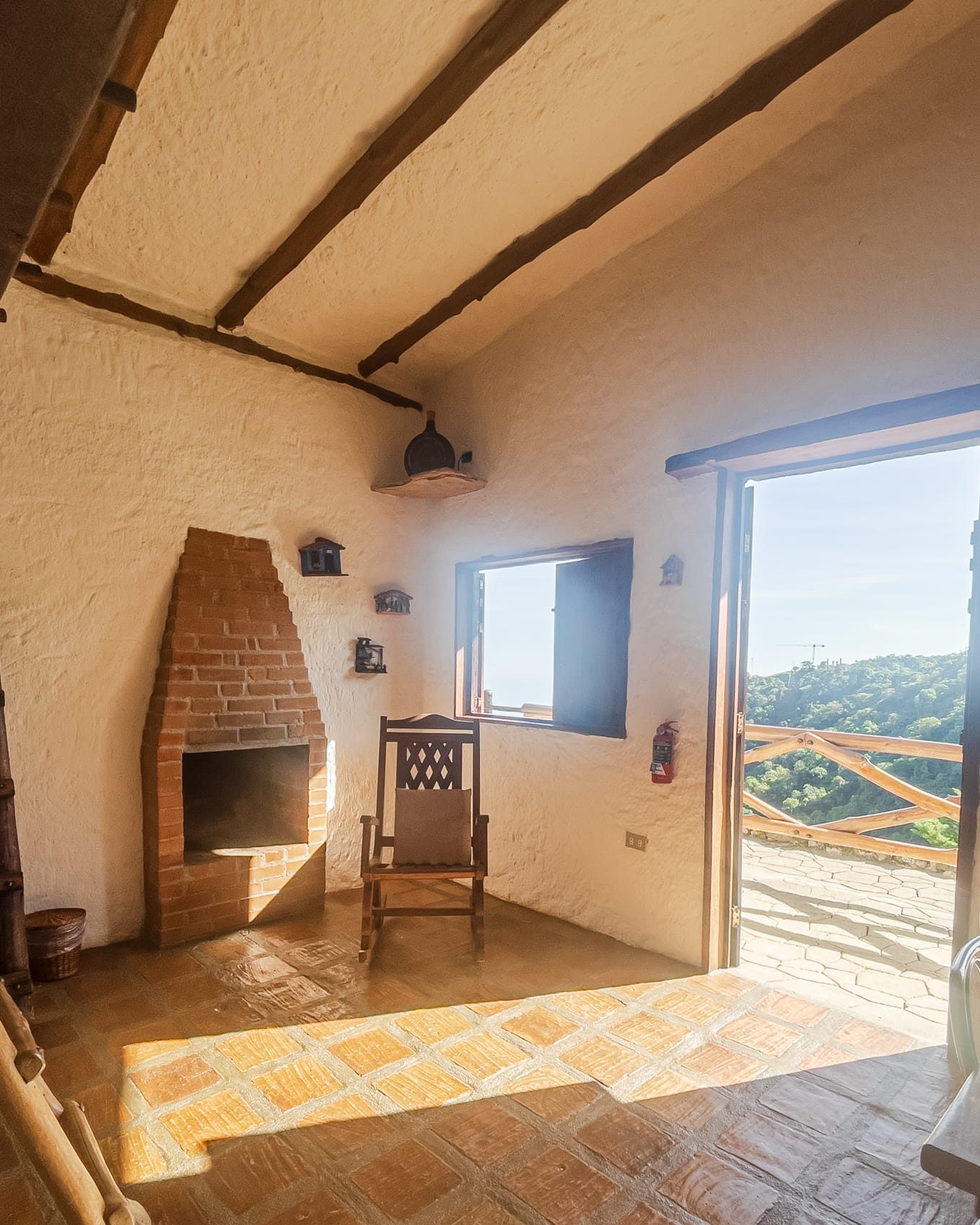 La chimenea de ladrillo y una mecedora reciben el sol que entra por la puerta abierta hacia la terraza