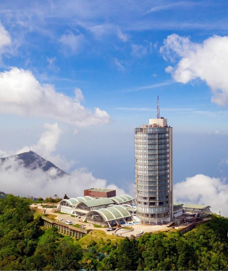 Vista aérea del Hotel Humboldt, torre cilíndrica sobre la cima de El Ávila entre nubes, junto a la estación del teleférico