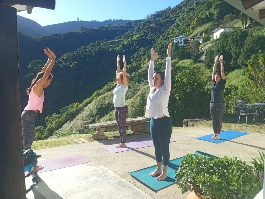 Cuatro mujeres estiran los brazos en postura de yoga sobre esterillas, en una terraza con vista a la montaña de Galipán.